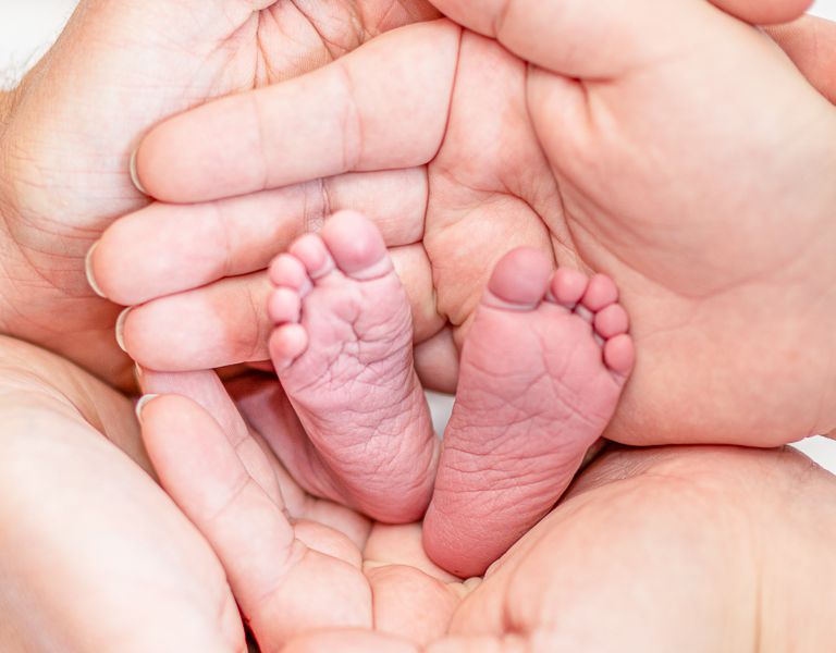 Das Bild zeigt Hände und Baby Füße, Eltern und ihr neugeborenes Kind