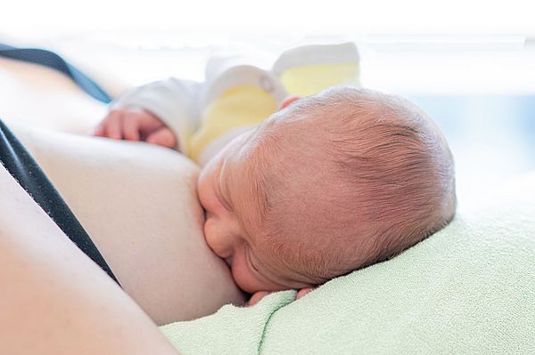 Das Bild zeigt ein Neugeborenes, das an der Brust der Mutter trinkt